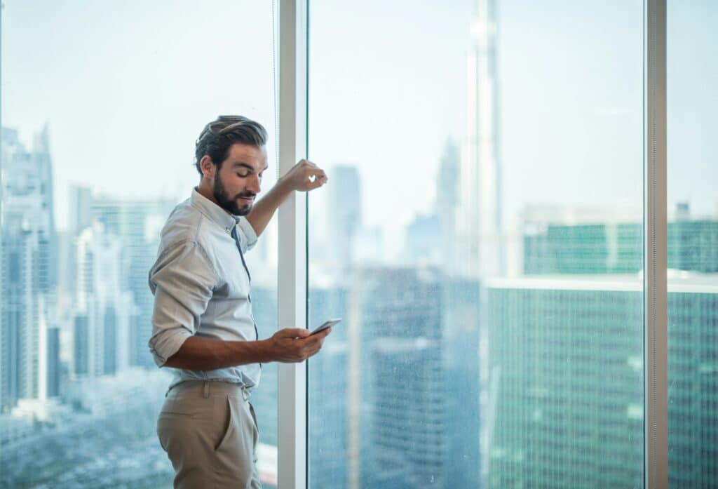 Geschäftsmann im Gebäude Glaswand schaut aufs Handy über news und aktuelles in Dubai