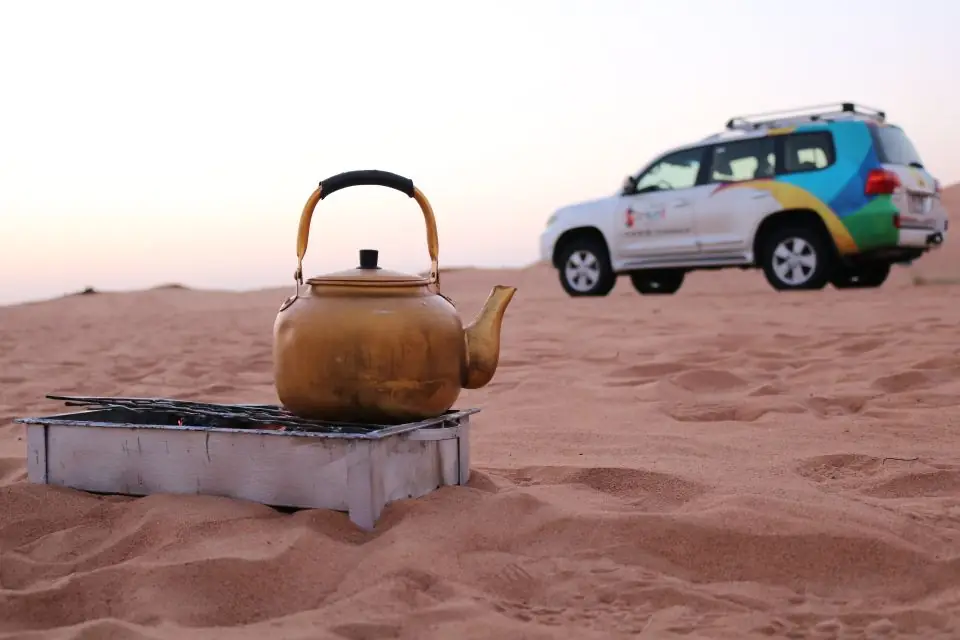 wüstensafari in dubai kaffeekanne in der wüste mit geländewagen im hintergrund